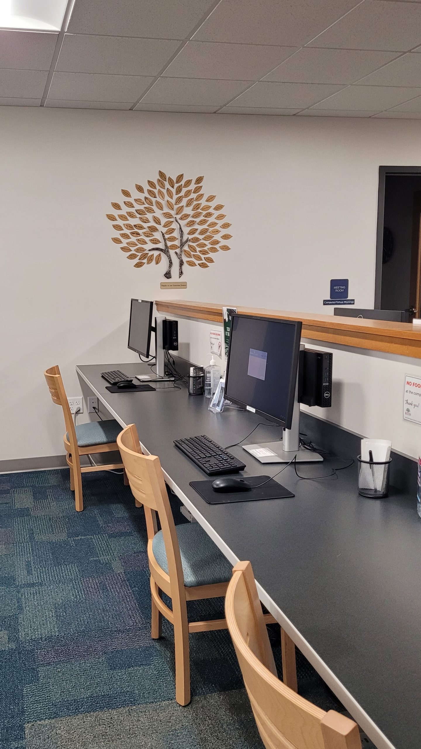 Computer station with chairs and monitors, and a decorative tree on the wall.